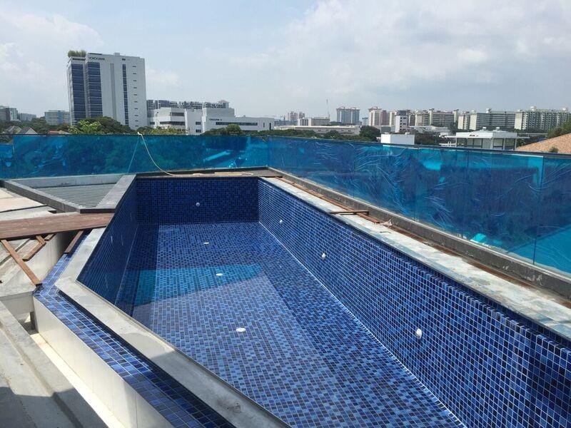 A rooftop swimming pool with blue-colored glass railings.